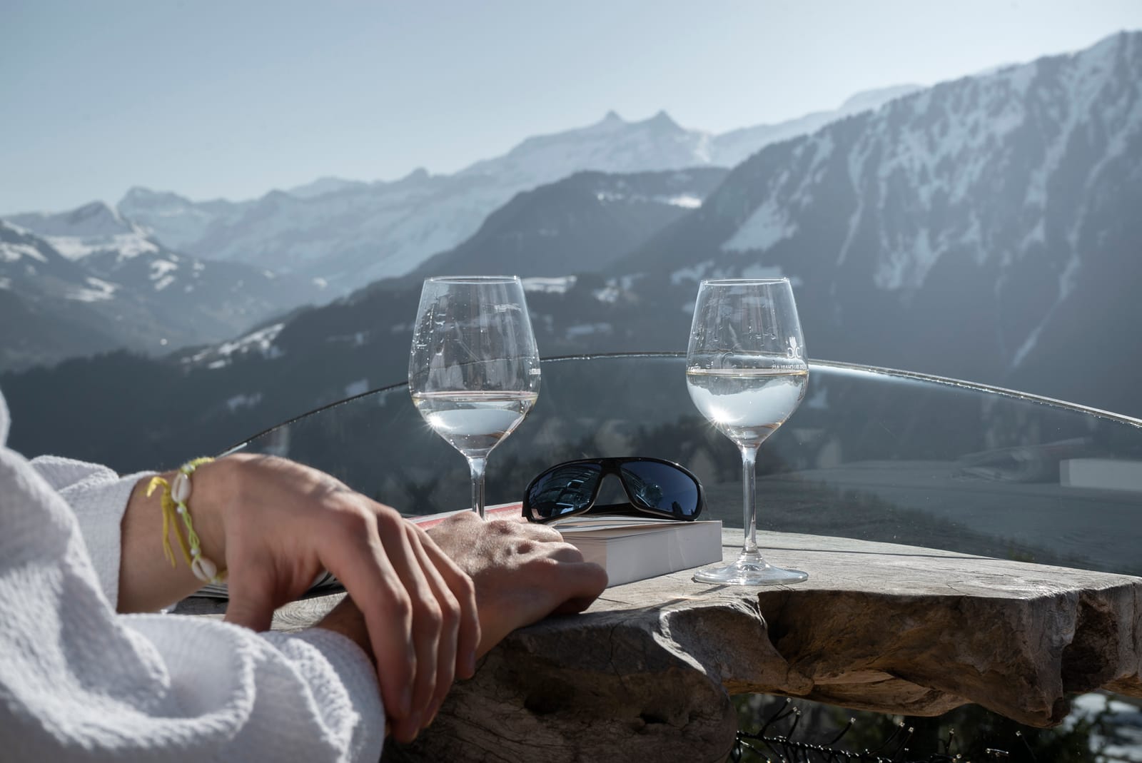 Verres et livre posés sur la table face au panorama alpin