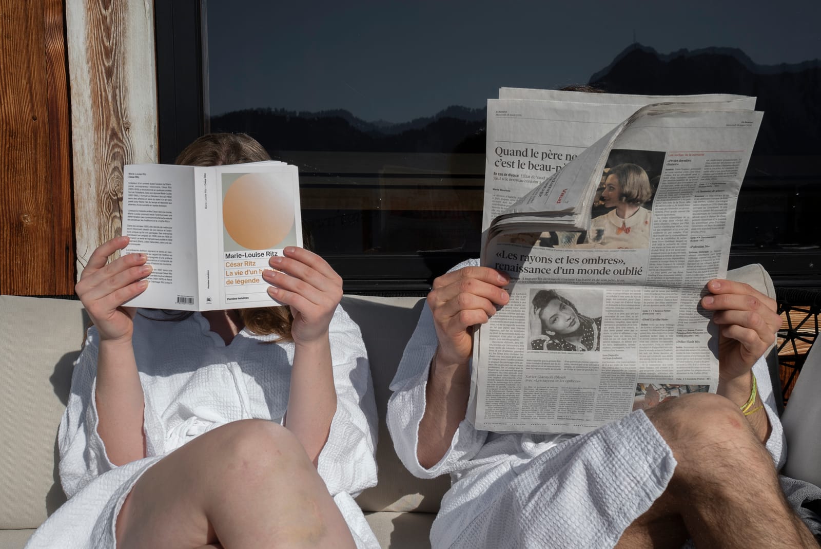 Couple lisant la presse en peignoirs sur la terrasse face aux Alpes